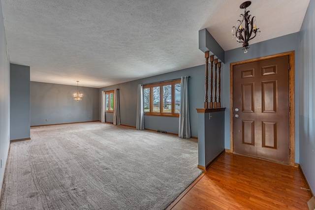 foyer entrance with a textured ceiling, a notable chandelier, carpet flooring, visible vents, and baseboards