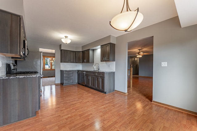 kitchen with stainless steel appliances, a sink, dark brown cabinets, light stone countertops, and light wood finished floors