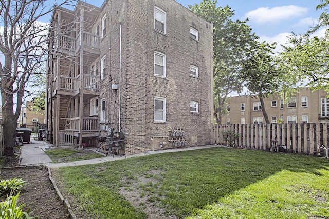 view of side of home featuring fence, a lawn, and brick siding