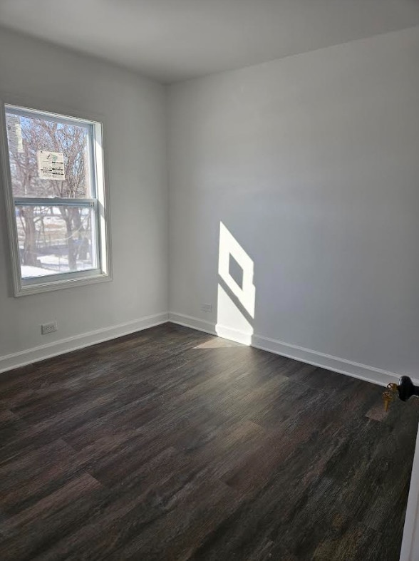 spare room featuring dark wood-type flooring and baseboards