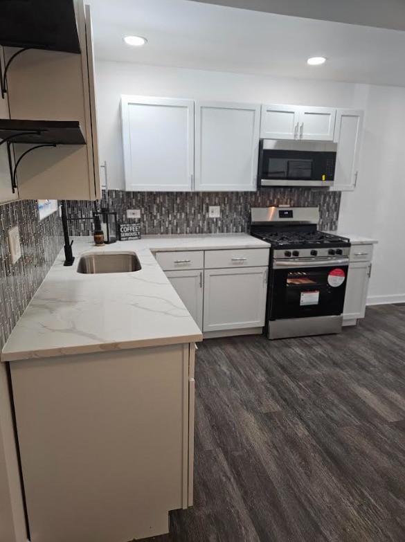 kitchen featuring light stone counters, dark wood finished floors, stainless steel appliances, tasteful backsplash, and white cabinetry