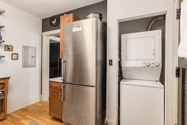 laundry room featuring stacked washing maching and dryer, light wood-type flooring, laundry area, electric panel, and baseboards