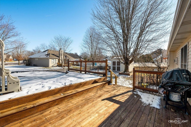 snow covered deck with a storage shed, area for grilling, a residential view, and an outdoor structure