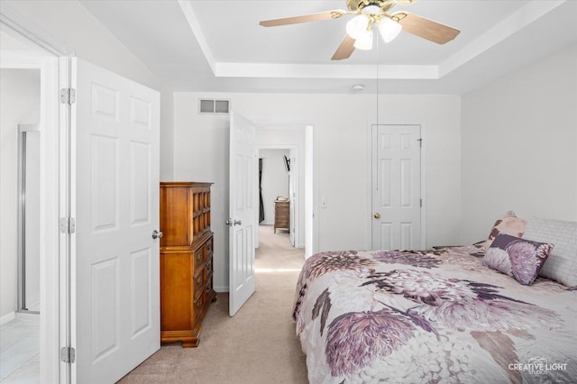 bedroom featuring light carpet, visible vents, a raised ceiling, and a ceiling fan