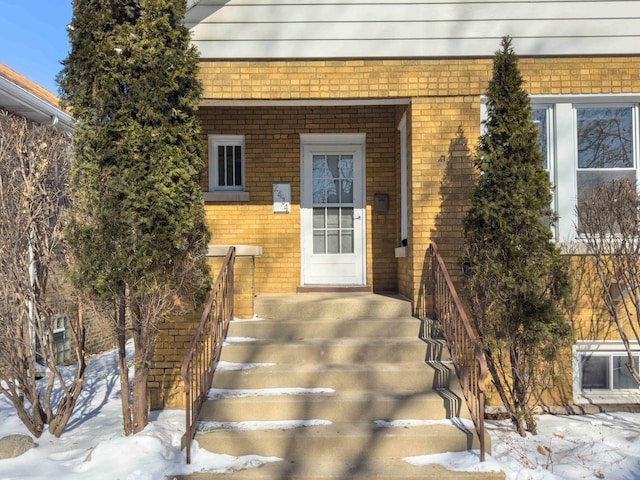 snow covered property entrance with brick siding