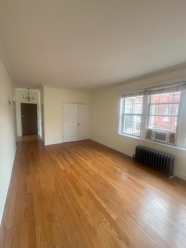 unfurnished bedroom with light wood finished floors, baseboards, radiator heating unit, ornamental molding, and cooling unit