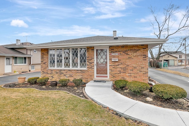 view of front of home featuring a front yard, brick siding, and roof with shingles