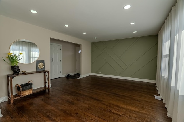 spare room featuring dark wood-style floors, an accent wall, visible vents, and recessed lighting