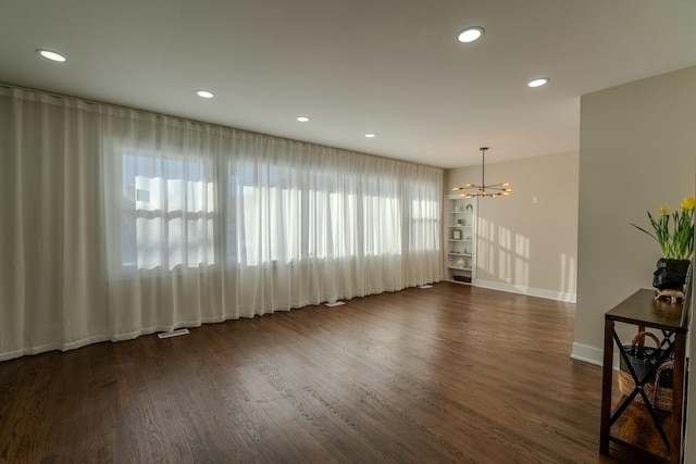 unfurnished room featuring baseboards, an inviting chandelier, dark wood finished floors, and recessed lighting