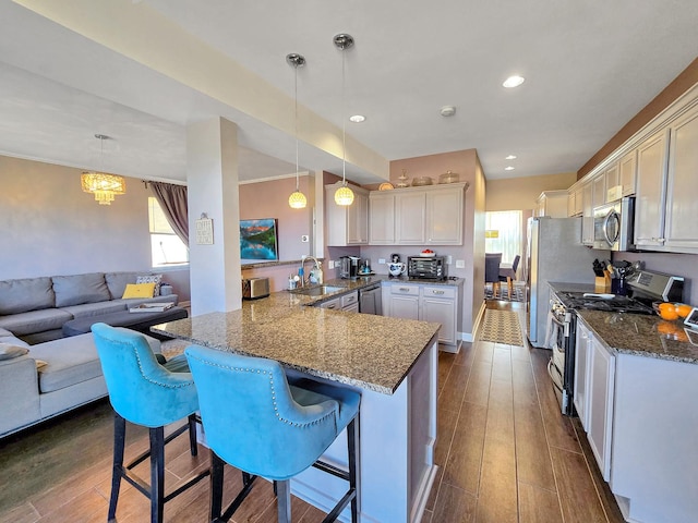 kitchen featuring a peninsula, appliances with stainless steel finishes, a breakfast bar area, and decorative light fixtures