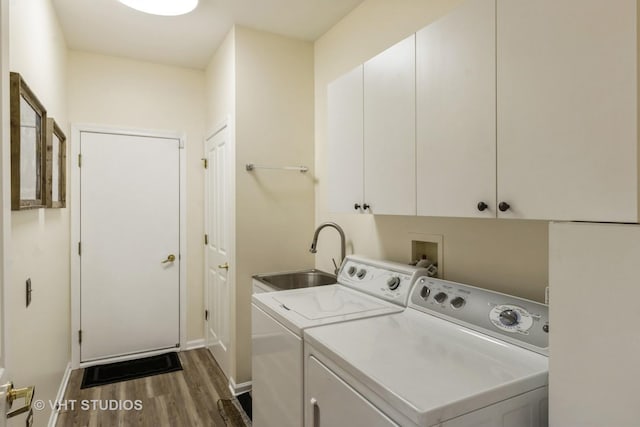 clothes washing area featuring washing machine and clothes dryer, cabinet space, a sink, wood finished floors, and baseboards