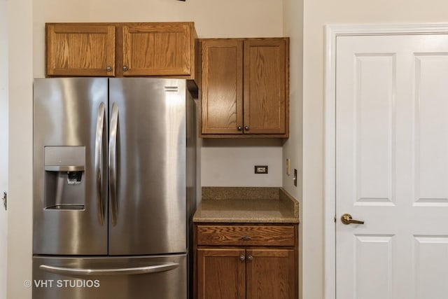 kitchen with brown cabinets, stainless steel fridge, and dark stone countertops