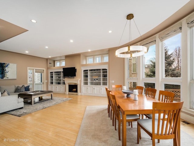 dining room featuring light wood finished floors, visible vents, built in features, a fireplace, and recessed lighting