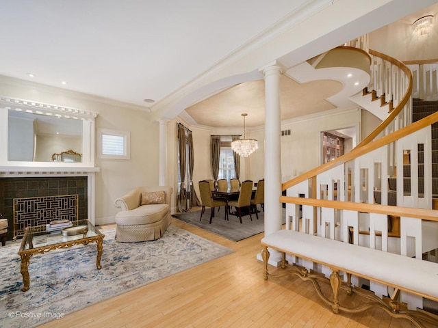 interior space with wood-type flooring, stairs, ornamental molding, a tiled fireplace, and ornate columns