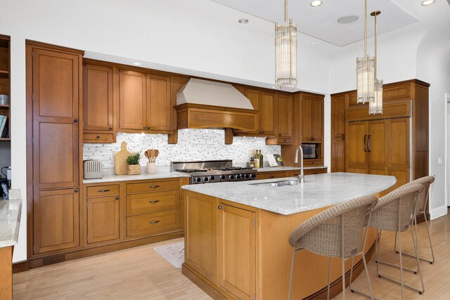 kitchen featuring light stone counters, light wood-style flooring, a sink, custom exhaust hood, and brown cabinetry