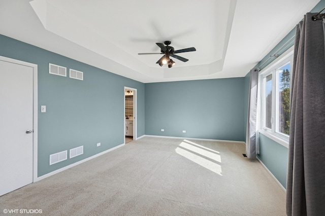 empty room with light carpet, baseboards, visible vents, a raised ceiling, and ceiling fan