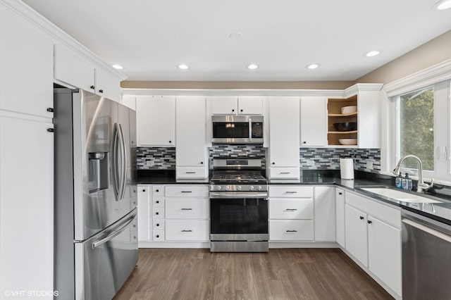 kitchen featuring dark countertops, stainless steel appliances, white cabinetry, open shelves, and a sink