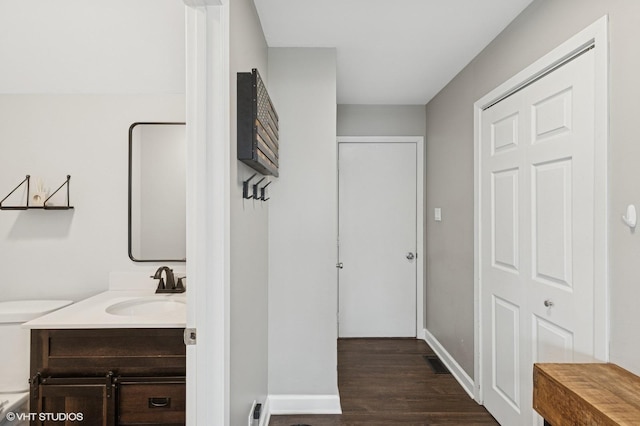 bathroom with a closet, toilet, vanity, wood finished floors, and baseboards