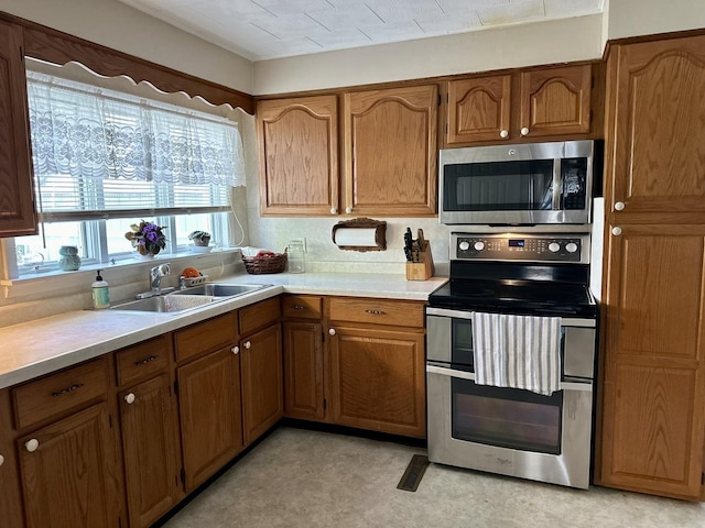 kitchen with brown cabinets, light floors, light countertops, appliances with stainless steel finishes, and a sink