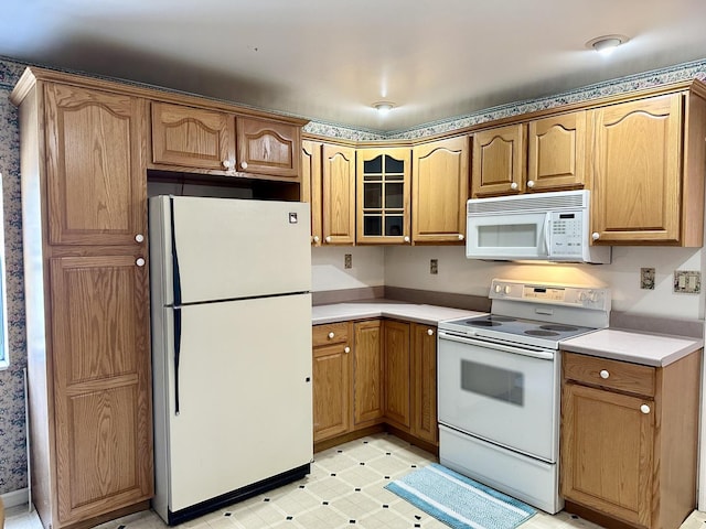 kitchen featuring light floors, light countertops, brown cabinetry, glass insert cabinets, and white appliances