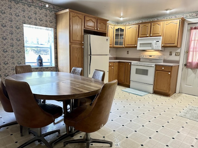 kitchen with white appliances, wallpapered walls, glass insert cabinets, light countertops, and light floors