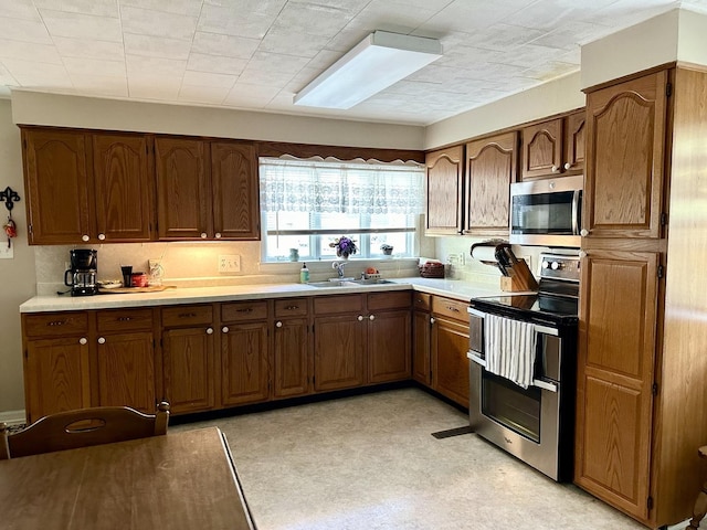 kitchen with a sink, stainless steel appliances, brown cabinetry, and light countertops