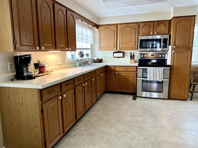 kitchen featuring a sink, light countertops, appliances with stainless steel finishes, brown cabinets, and light floors