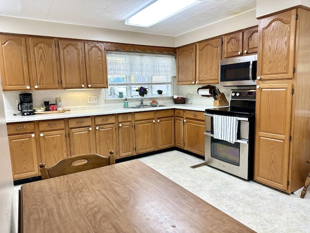 kitchen with a sink, light countertops, appliances with stainless steel finishes, brown cabinets, and light floors