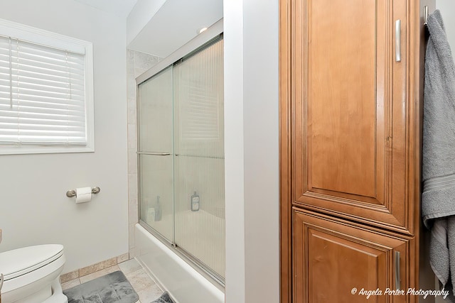 full bath featuring baseboards, combined bath / shower with glass door, and toilet