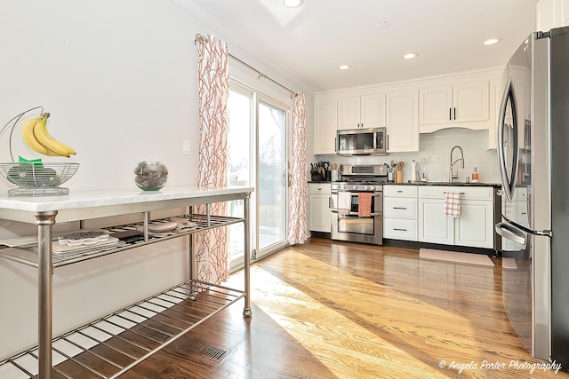 kitchen with dark countertops, light wood-style flooring, decorative backsplash, appliances with stainless steel finishes, and a sink