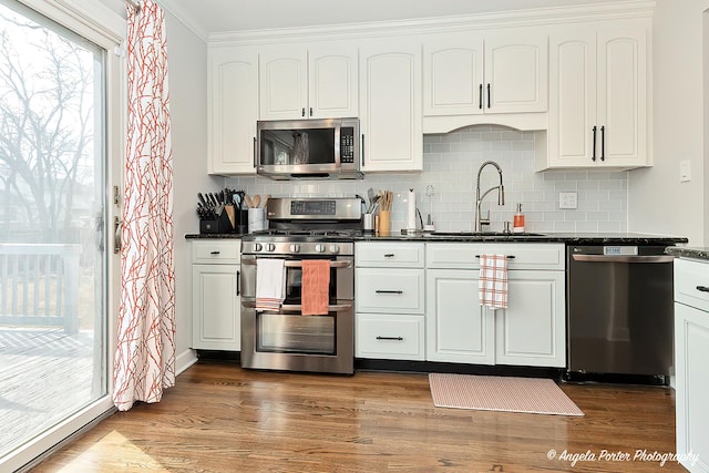 kitchen featuring stainless steel appliances, wood finished floors, dark countertops, and a sink