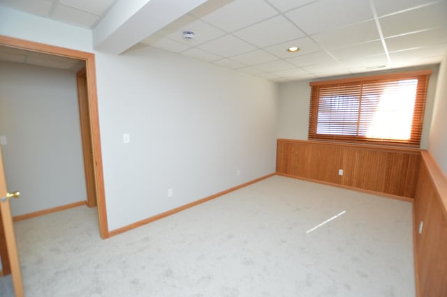 carpeted empty room with a paneled ceiling, baseboards, wood walls, and wainscoting