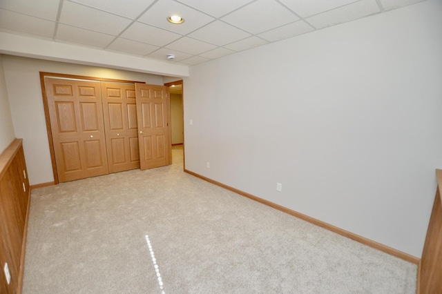 unfurnished bedroom with light colored carpet, a closet, a drop ceiling, and baseboards