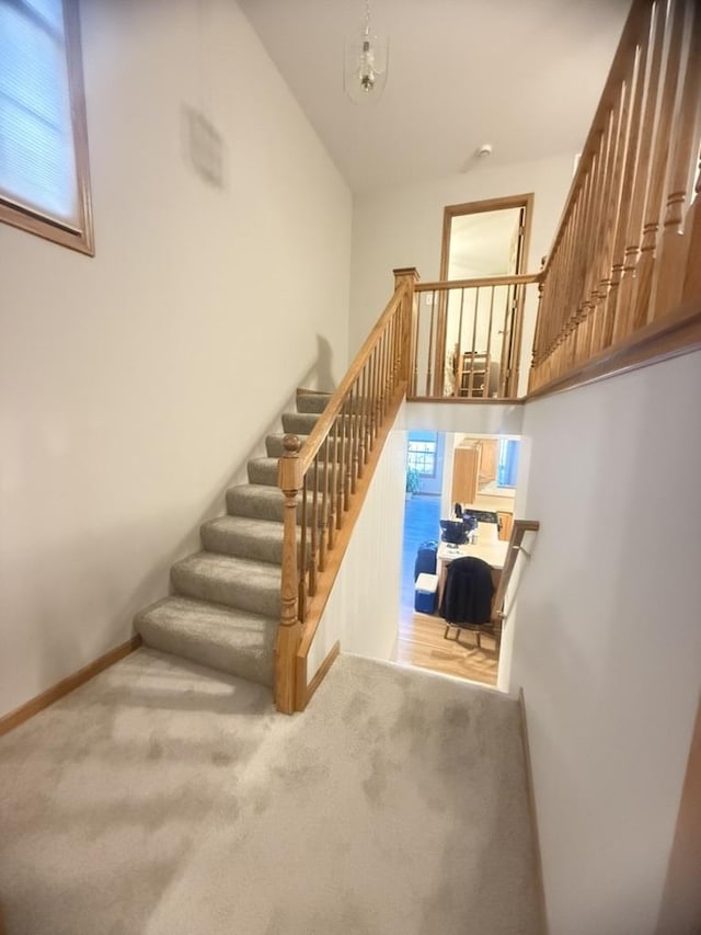 stairway featuring baseboards, a towering ceiling, and carpet flooring