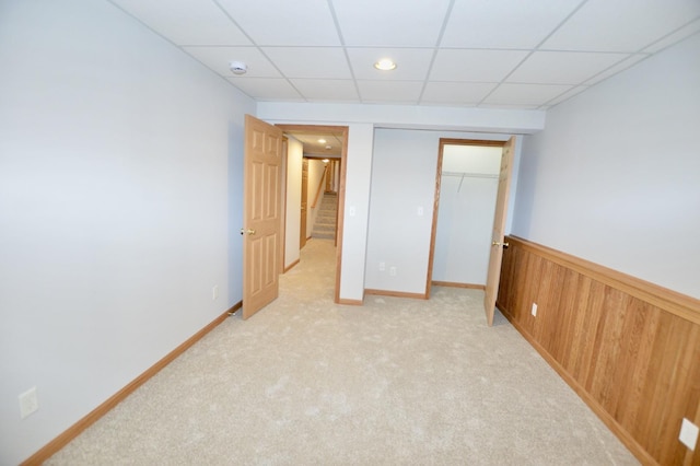 unfurnished bedroom featuring wooden walls, a wainscoted wall, light carpet, a closet, and a paneled ceiling