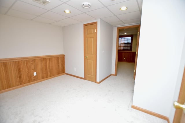 unfurnished room with visible vents, a drop ceiling, wooden walls, wainscoting, and light colored carpet