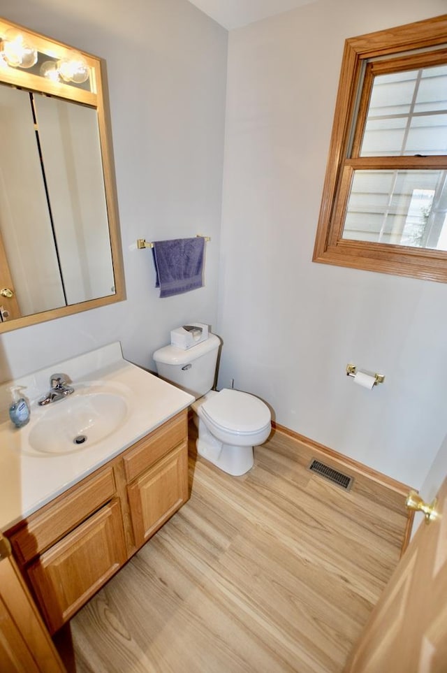 half bathroom with visible vents, baseboards, toilet, wood finished floors, and vanity