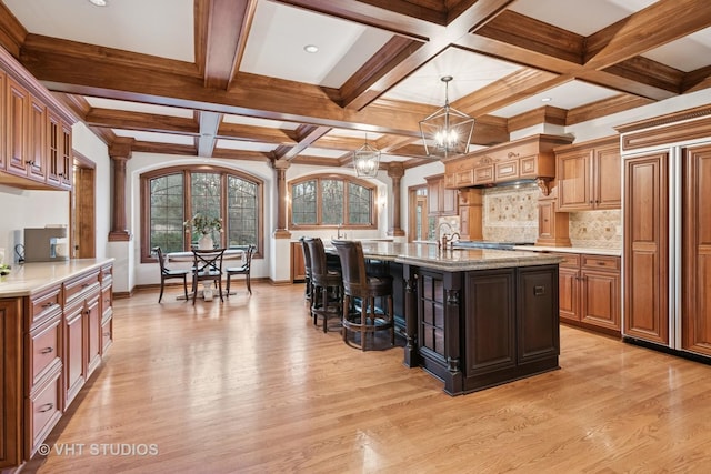 kitchen featuring a breakfast bar area, light wood-style flooring, an island with sink, glass insert cabinets, and pendant lighting