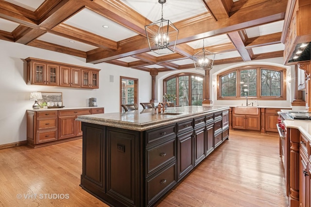 kitchen featuring a kitchen island with sink, a sink, hanging light fixtures, light wood-type flooring, and glass insert cabinets