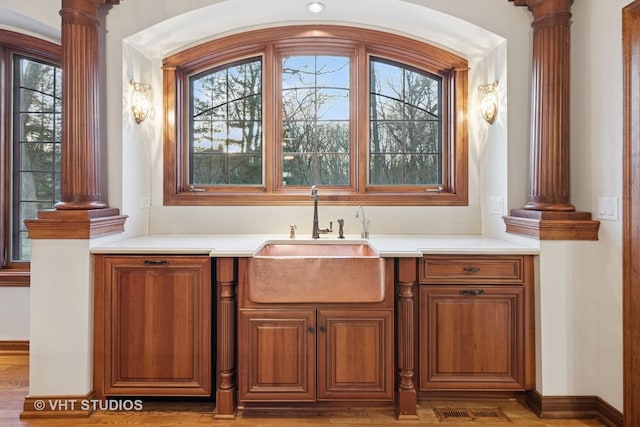 bar featuring wood finished floors, a sink, and ornate columns