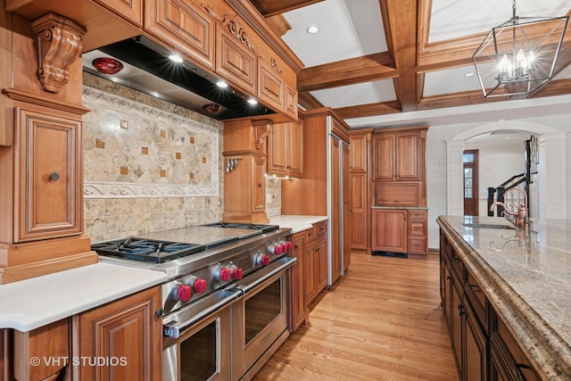 kitchen featuring arched walkways, brown cabinets, ventilation hood, double oven range, and a sink