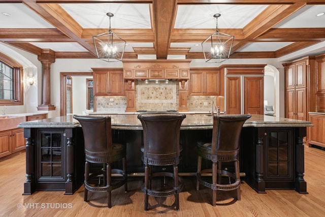 kitchen with a large island, hanging light fixtures, brown cabinetry, light stone countertops, and a chandelier