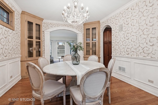 dining area featuring arched walkways, dark wood-style flooring, a wainscoted wall, and wallpapered walls