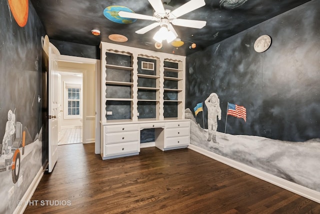 unfurnished office featuring ceiling fan, dark wood-type flooring, built in features, baseboards, and built in desk