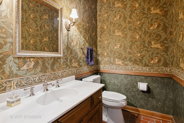 half bath with toilet, wallpapered walls, a wainscoted wall, and vanity