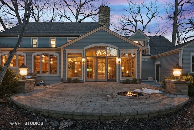 back of property at dusk featuring a fire pit, a chimney, and a patio area