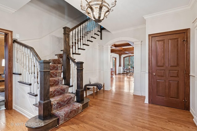 foyer entrance featuring arched walkways, a decorative wall, coffered ceiling, light wood-type flooring, and beam ceiling