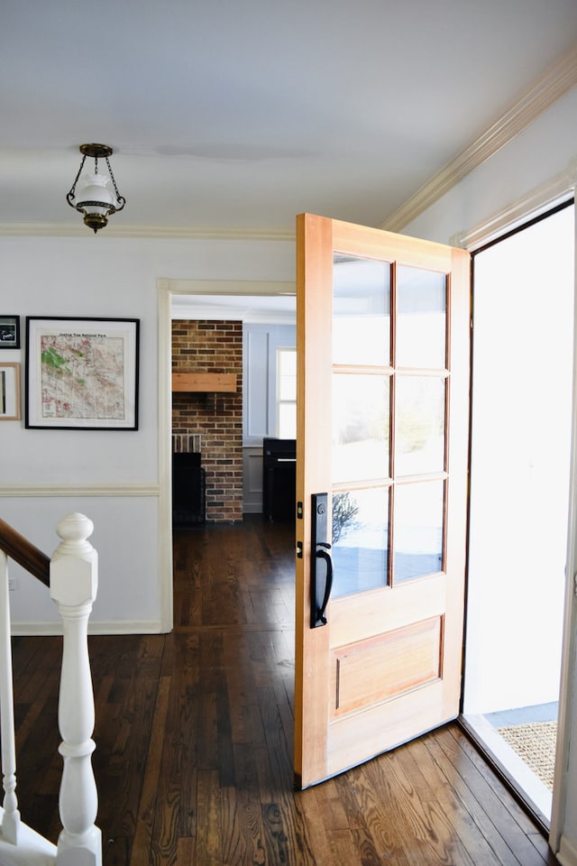 interior space with ornamental molding, a brick fireplace, and dark wood finished floors