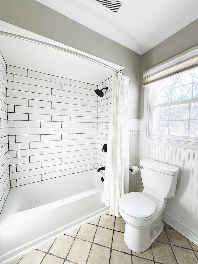 bathroom featuring tile patterned flooring, toilet, visible vents, wainscoting, and shower / tub combo with curtain