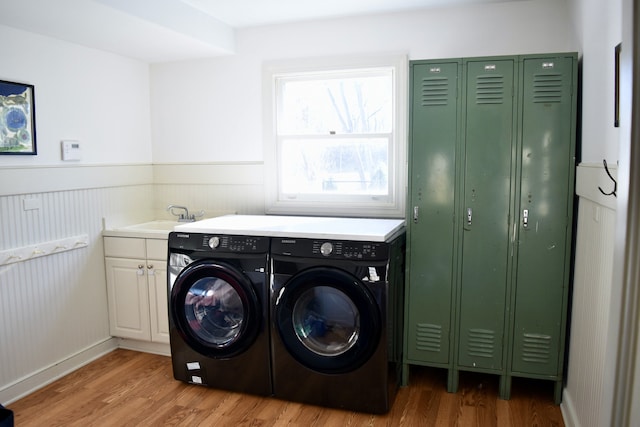 laundry room featuring cabinet space, light wood finished floors, washer and clothes dryer, a wainscoted wall, and a sink